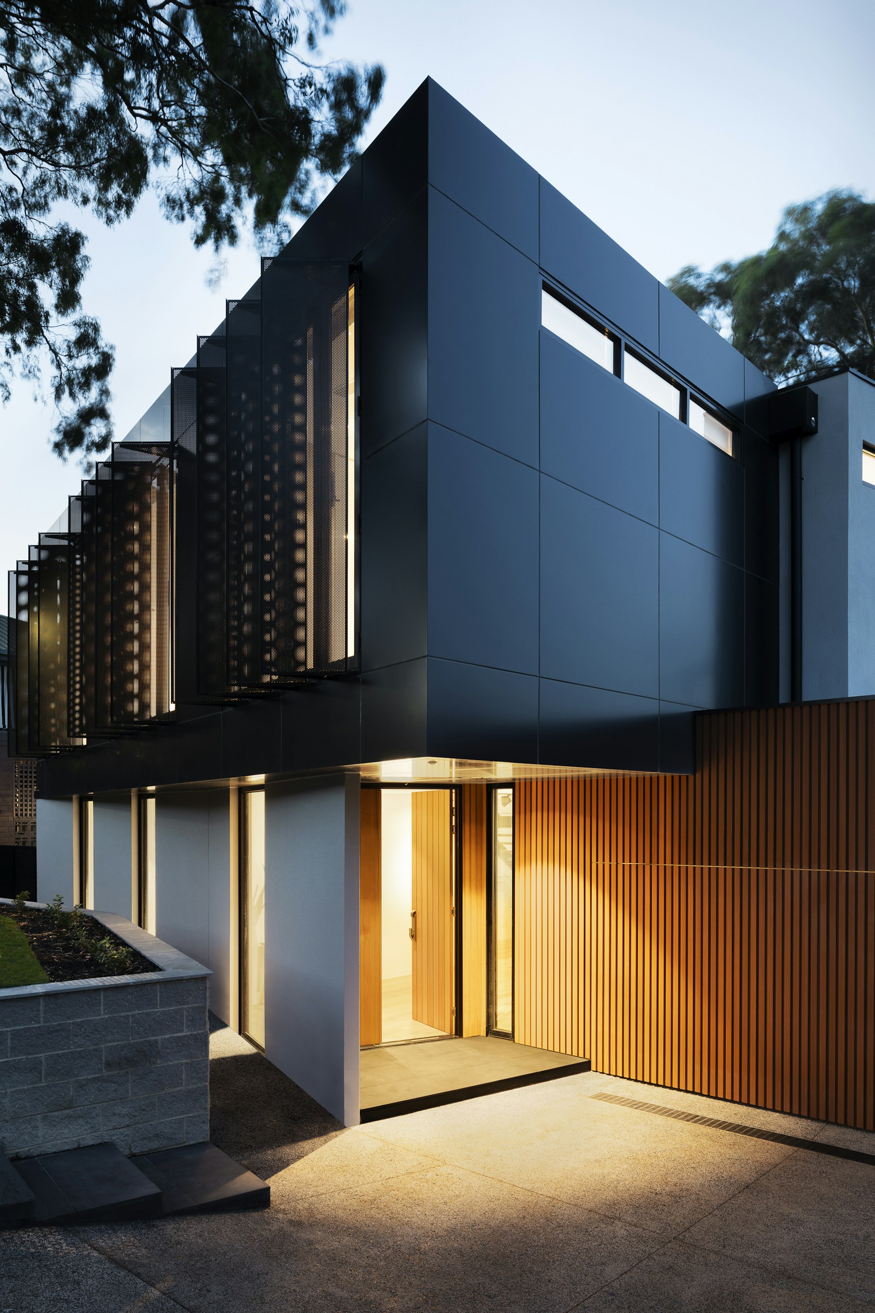Sculptural dark home entrance glowing at twilight